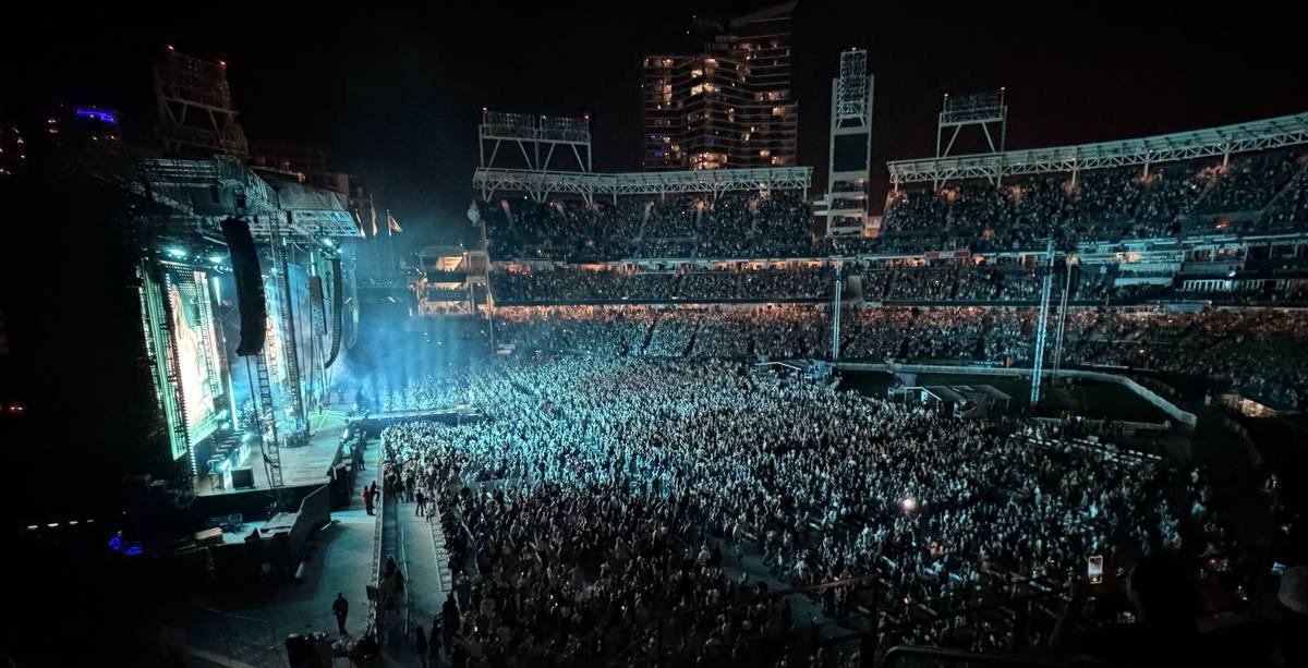 A packed ballpark at night, stage at left, the floor and every deck full.